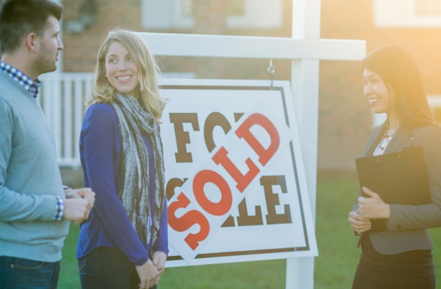 First-time homeowners and realtor standing in front of sold sign.